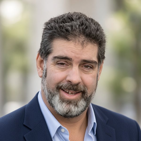 Cam Slater, New Zealand writer and publisher, smiling, in a navy blazer and light blue shirt.